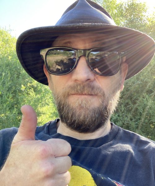 Man with sunglasses and hat giving thumbs-up.